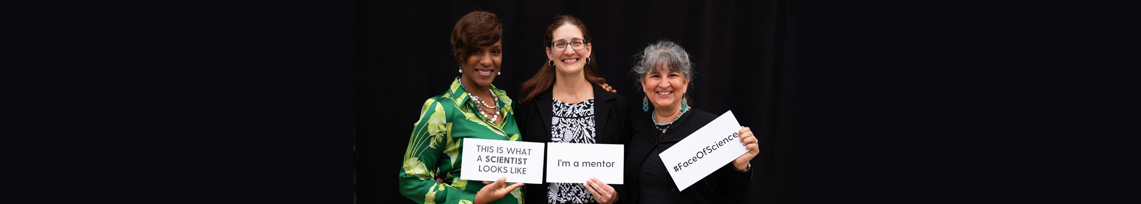 Three people who are each holding a sign. Each sign says: This is what a scientist looks like, I'm a mentor, and hashtag FaceOfScience.